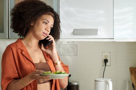 Téléchargez les photos : Femme sérieuse avec assiette de salade de légumes appelant un ami ou un membre de la famille - en image libre de droit