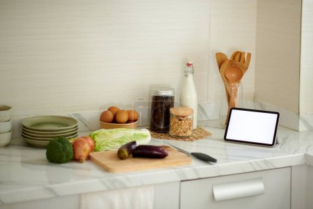 Téléchargez les photos : Tablette numérique avec écran vide sur le comptoir de cuisine à côté des légumes préparés pour la cuisson - en image libre de droit