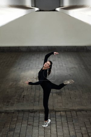 Foto de Retrato de joven bailarina en negro de pie en pose elegante durante el baile en la calle - Imagen libre de derechos