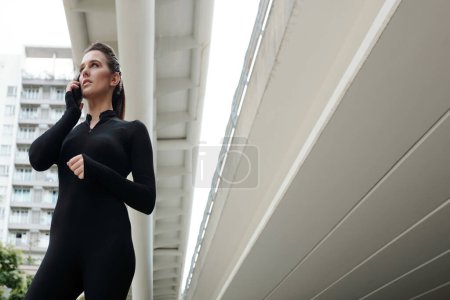 Photo for Young dance girl in black suit talking on mobile phone while standing in the city - Royalty Free Image