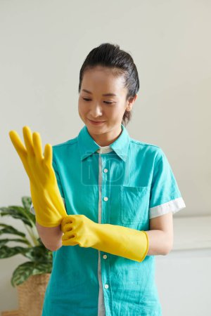 Foto de Asiático joven limpiador poner en uniforme y guantes de goma listo para trabajar - Imagen libre de derechos
