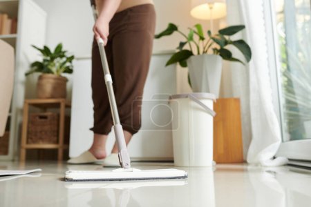 Téléchargez les photos : Gros plan de la femme au foyer utilisant la serpillière pour laver le sol dans la chambre, elle fait le nettoyage humide - en image libre de droit