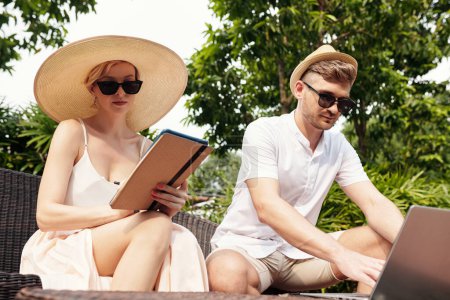 Photo for Young adult Caucasian man and woman spending summer day outdoors working or surfing Internet on digital tablet and laptop - Royalty Free Image