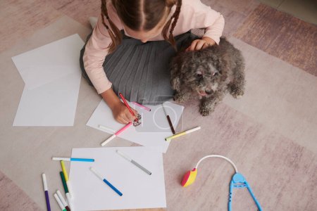 Photo for Preteen girl sitting on floor and drawing her small dog, view from above - Royalty Free Image