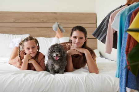 Photo for Mother, daughter and little dog lying in bed and smiling at camera - Royalty Free Image