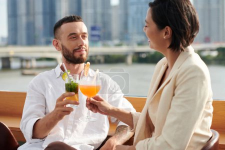 Photo for Smiling young man enjoying drinks and conversation with woman at rooftop bar - Royalty Free Image