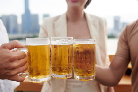 Photo for Close-up image of people toasting with big mugs of cold beer at rooftop pub - Royalty Free Image