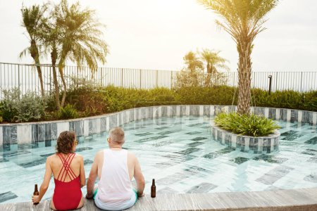 Photo for Middle-aged couple sitting by rooftop swimming pool, drinking beer and enjoying sunset - Royalty Free Image