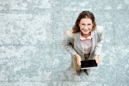 Photo for Cheerful middle-aged businesswoman holding tablet computer and looking up at camera - Royalty Free Image
