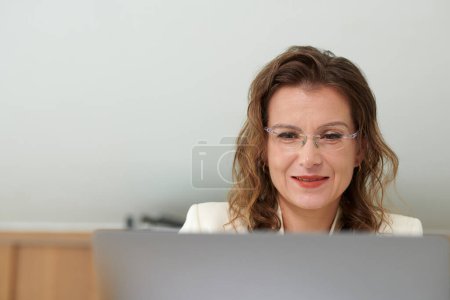 Photo for Portrait of smiling mature businesswoman reading article on laptop screen - Royalty Free Image