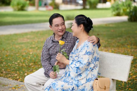 Photo for Smiling senior man hugging wife and giving her yellow rose - Royalty Free Image
