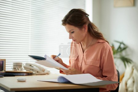 Photo for Serious mature businesswoman correcting data in report when working in office - Royalty Free Image