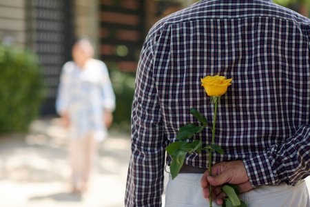 Photo for Senior man hiding yellow rose behind back as present for girlfriend - Royalty Free Image