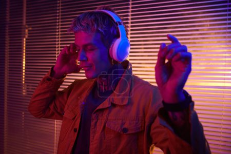 Photo for Young man dancing to music in headphones in neon bedroom - Royalty Free Image
