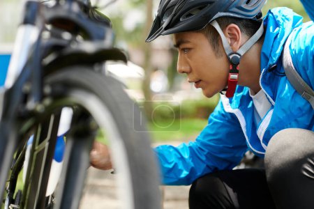 Téléchargez les photos : Inquiet jeune homme asiatique vérifier les pneus de vélo avant de faire un long trajet - en image libre de droit