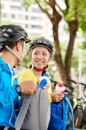 Photo for Positive young couple taking water bottles out of backpacks to drink after long bicycle ride - Royalty Free Image