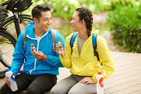 Téléchargez les photos : Heureux jeune couple manger des barres d'énergie après une balade à vélo pour obtenir plus d'énergie - en image libre de droit