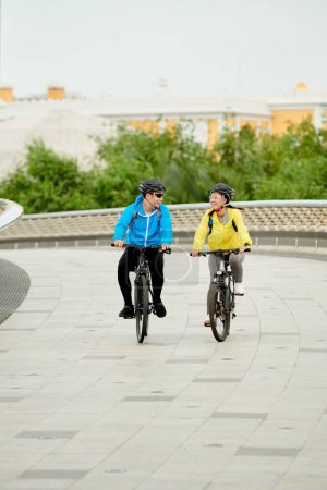 Photo for Happy couple in protective helmets riding bicycles along bridge - Royalty Free Image