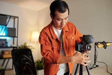 Foto de Serious joven ininfluencer configuración de equipos de filmación en su estudio en casa - Imagen libre de derechos
