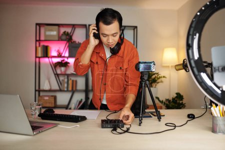 Photo for Young blogger preparing for streaming, setting shooting equipment and checking sound - Royalty Free Image