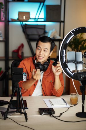 Téléchargez les photos : Jeune blogueur technologique asiatique filmant des écouteurs examen pour les médias sociaux - en image libre de droit