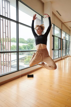 Foto de Bailarina femenina delgada saltando en el aire cuando baila en estudio con música en altavoz - Imagen libre de derechos