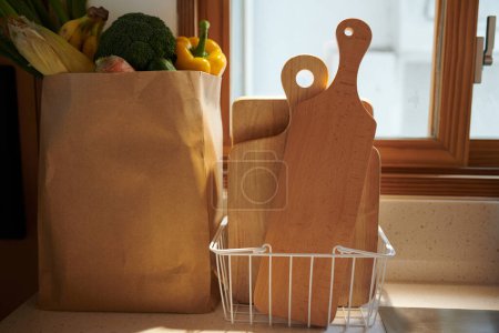 Téléchargez les photos : Panier en métal avec planches à découper en bois à côté du paquet d'épicerie sur le comptoir dans la cuisine - en image libre de droit