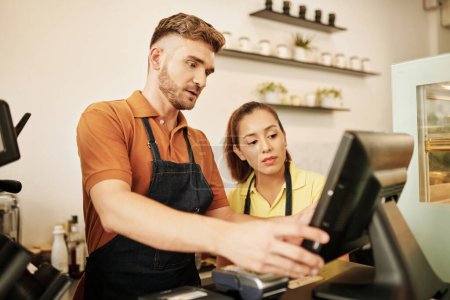 Téléchargez les photos : Coffeeshop barista expliquant aux nouveaux travailleurs comment utiliser la caisse enregistreuse - en image libre de droit