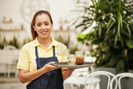 Photo for Portrait of smiling waitress holding tray with cold water and iced coffee for customer - Royalty Free Image