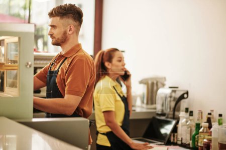 Téléchargez les photos : Coffeeshop barista faire du café lorsque le propriétaire commande des fournitures jetables par téléphone - en image libre de droit