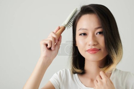 Foto de Retrato de estudio de una joven alegre cepillando el cabello y sonriendo a la cámara - Imagen libre de derechos