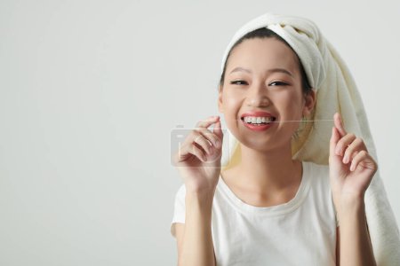 Téléchargez les photos : Jeune femme glissant doucement fil dentaire entre la gomme et les dents après la douche - en image libre de droit