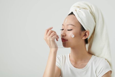 Photo for Smiling young woman closing eyes and applying renewing lotion after morning shower - Royalty Free Image