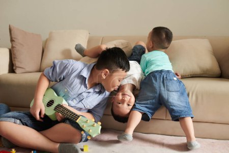 Photo for Preteen boy playing ukulele and kissing younger brother - Royalty Free Image