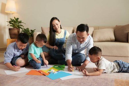 Photo for Smiling parents and their three sons drawing pictures on floor together - Royalty Free Image
