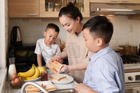 Foto de Las manos de la madre enseñando a los hijos cómo lanzar mermelada en tostadas para el desayuno - Imagen libre de derechos