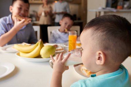 Téléchargez les photos : Petit garçon boire un verre de lait à la table du petit déjeuner - en image libre de droit
