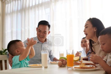 Téléchargez les photos : Petit garçon racontant l'histoire à sa famille pendant le petit déjeuner - en image libre de droit