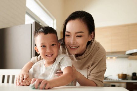 Photo for Smiling mother teaching son cleaning table after dinner - Royalty Free Image