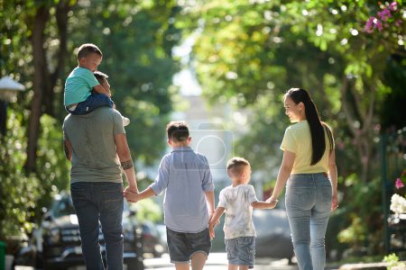 Téléchargez les photos : Heureuse famille de cinq personnes marchant dans la rue ensemble par une journée ensoleillée, vue de derrière - en image libre de droit