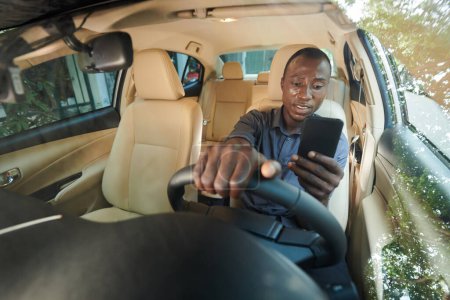 Téléchargez les photos : Distacted anxieux homme lisant des notifications sur smartphone lors de la conduite de voiture - en image libre de droit