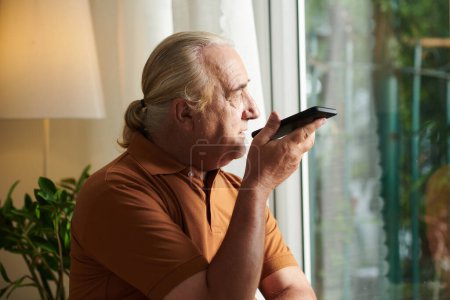 Photo for Portrait of aged man with ponytail recording voice message on smartphone - Royalty Free Image