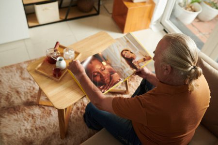 Téléchargez les photos : Homme âgé regardant des photos dans l'album publié par le photographe - en image libre de droit