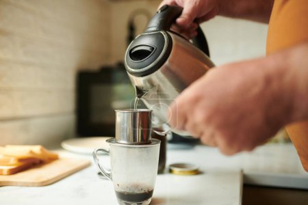 Closeup image of man pouring hot water in phin filter when making cup of coffee at home