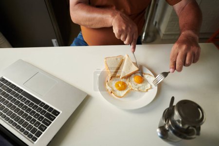 Téléchargez les photos : Image recadrée d'un homme âgé ayant deux œufs frits avec du pain et du café pour le petit déjeuner - en image libre de droit