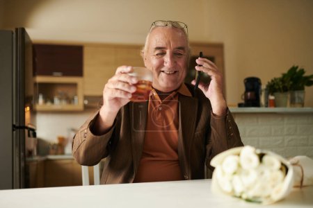 Téléchargez les photos : Heureux mais anxieux homme âgé boire un verre de whisky avant le premier rendez-vous pour obtenir un peu de courage - en image libre de droit