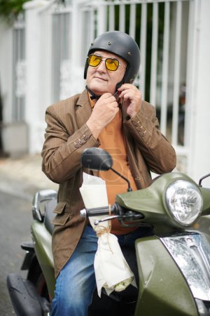 Foto de Hombre mayor con gafas de sol amarillas y casco protector al montar en scooter en la ciudad - Imagen libre de derechos