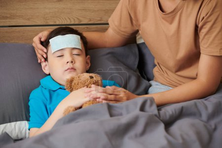 Photo for Sick preteen boy hugging teddy bear when sleeping in bed - Royalty Free Image