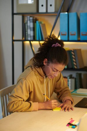 Foto de Colegiala escribiendo palabras difíciles en notas adhesivas al estudiar para el examen en casa - Imagen libre de derechos