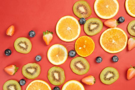 Photo for Orange and kiwi slices and various berries on red background - Royalty Free Image